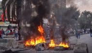 Lebanese anti-government protesters stand behind a burning barricade during a demonstration in Beddawi town on the outskirts of the northern Lebanese port city of Tripoli on October 26, 2019. (AFP / Fathi AL-MASSRI)