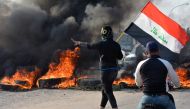 A demonstrator holds an Iraqi flag near burning tires during ongoing anti-government protests in Nassiriya, Iraq November 24, 2019. REUTERS/Ahmed Dhahi 