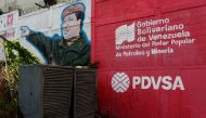 The logo of the Venezuelan state oil company PDVSA is seen next to a mural depicting late President Hugo Chavez at a gas station in Caracas, March 2, 2017. Reuters / Carlos Garcia Rawlins