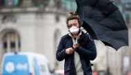 A man wearing a protective face mask walks with an umbrella in London, Britain, March 5, 2020. Reuters/Henry Nicholls