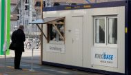 A man waits in front of a container of Medbase medical center, used for tests on coronavirus disease (COVID-19) on a square in Winterthur, Switzerland March 24, 2020. REUTERS/Arnd Wiegmann