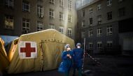 Health workers wearing face mask stand in front of a triage tent for suspected COVID-19 patients outside the Santa Maria Hospital in Lisbon on April 2, 2020.   AFP / PATRICIA DE MELO MOREIRA