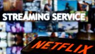 A smartphone with the Netflix logo lies in front of displayed 