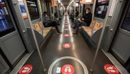Commuters maintaining distance sit next to seats with stickers reading 