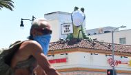A cyclist wearing facial covering rides past the dinosaur atop the 