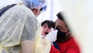 Jose Vatres (R) holds his son Aidin who reacts as nurse practitioner Alexander Panis (L) takes a nasal swab sample to test for COVID-19 at a mobile testing station in a public school parking area in Compton, California, just south of Los Angeles, on April