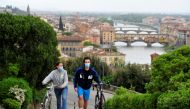 People wearing protective face masks push their bicycles during the lockdown, ahead of Italy's gradual lifting of restrictions which begins from May 4, due to the spread of the coronavirus disease (COVID-19), in Florence, Italy, May 1, 2020. REUTERS/Jenni