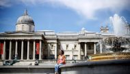 A woman enjoys the sunshine by water fountains in Trafalgar Square in central London on May 18, 2020. AFP / Tolga Akmen 
