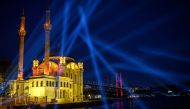 TOPSHOT - A picture taken on May 19, 2020 shows the Bosphorus bridge and the Ortakoy mosque as a light shine over the Bosphorus to mark the Youth and Sports Day in Istanbul during a four-day curfew aimed at curbing the spread of the COVID-19 pandemic, cau