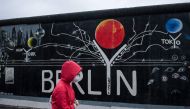 A woman with a protective face mask passes a mural on parts of former Berlin Wall at East Side Gallery in Berlin, on June 20, 2020. / AFP / STEFFI LOOS
