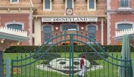 (FILES) In this file photo an employee cleans the grounds behind the closed gates of Disneyland Park on the first day of the closure of Disneyland and Disney California Adventure theme parks as fear of the spread of coronavirus continue, in Anaheim, Calif