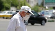A pedestrian wearing a protective mask and a shield due to the COVID-19 coronavirus, walks along a street in the Iranian capital Tehran on June 28, 2020. AFP / ATTA KENARE
