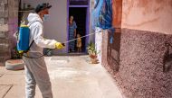 A woman and a child confined at home watch a Moroccan municipal worker disinfect their street in the southern port city of Safi on June 9, 2020, during a total lockdown ordered by the authorities following the discovery of several new cases of COVID-19 co