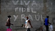 Afro-Cubans wear face masks as a preventive measure against the spread of the novel coronavirus, COVID-19, as they walk past a graffiti reading 