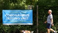 A man walks his dog past a poster promoting the coronavirus disease (COVID-19) testing at local mobile test centres, in Hounslow, London, Britain August 4, 2020. REUTERS/Toby Melville