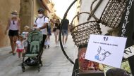 Tourists with protective masks walk past a sign reading 'mask is mandatory' in the streets of the old city of Bonifacio on August 5, 2020 on the French Mediterranean island of Corsica, the first and only city in Corsica where the mask is mandatory in the 