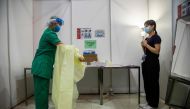 A medical worker (L) demonstrates removing her gown while being supervised in an area where protective gear is put on and taken off at a temporary field hospital set up at Asia World Expo in Hong Kong on August 1, 2020. / AFP / ISAAC LAWRENCE