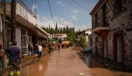 People clean in a destroyed street following a storm at the village of Politika, on Evia island, northeast of Athens, on August 9, 2020. Five people including a baby died and two more were missing as torrential rains and floods swept the Greek island of E