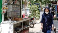A woman clad in mask due to COVID-19 coronavirus pandemic walks past a newspaper stall in Iran's capital Tehran on August 15, 2020.  AFP 
