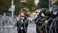 A woman uses a camera next to law enforcement officers standing behind barbed wire during an opposition demonstration to protest against presidential election results, in Minsk, Belarus August 23, 2020. REUTERS/Vasily Fedosenko