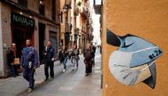 FILE PHOTO.People pass near a drawing of a person wearing a mask in a wall, due to the coronavirus outbreak, in central Barcelona, Spain, March 12, 2020. REUTERS/Albert Gea
