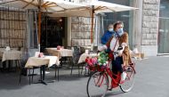 A woman wearing a protective face mask rides a bicycle past a restaurant as the outbreak of the coronavirus disease (COVID-19) continues, in Rome, Italy, October 25, 2020. REUTERS/Yara Nardi
