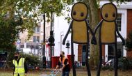 Staff working for British street artist STIK move bundles of local newspapers containing free copies of his artwork to be given away to local residents, during the unveiling of his bronze sculpture 