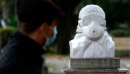 A man wearing a face mask walks by a marble bust dedicated to doctors, nurses and health workers untitled 