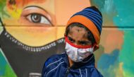 A boy wearing a facemask as a preventive measure against the Covid-19 coronavirus walks past a mural in New Delhi on November 23, 2020. / AFP / Sajjad HUSSAIN