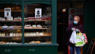 A customer wearing a face mask or covering due to the COVID-19 pandemic, carries her shoppingas she leaves a patisserie in Sittingbourne in the Swale district of Kent, south east England on November 24, 2020, which has become England's worst hit coronavir