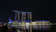People sit along the steps of the quay watching lights illuminate Marina Bay Sands hotels and resorts to celebrate its tenth anniversary and usher in the holiday season in Singapore on November 26, 2020. / AFP / Roslan Rahman