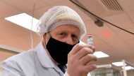 Britain's Prime Minister Boris Johnson, wearing a hair net and face covering, poses for a photograph with a vial as he views the last minute quality testing of the 'fill and finish' stage of the manufacturing process of COVID-19 vaccines, Wales, Britain N