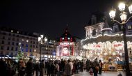 People gather near a merry-go-round on the Place de l'Hotel de Ville in Paris, where the city has set up a christmas village, on December 26, 2020. / AFP / Thomas SAMSON