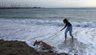 A woman plays with a dog on a beach during an unusual warm day, amid the coronavirus disease (COVID-19) pandemic, in Athens, Greece, January 10, 2021. REUTERS/Costas Baltas
