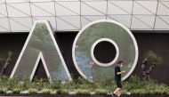 A man wearing a protective face mask walks past an Australian Open logo in Melbourne Park. Reuters/Loren Elliott