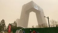 Construction workers are seen in front of the CCTV headquarters shrouded in dust as the city is hit by a sandstorm, in Beijing, China March 28, 2021. REUTERS/Martin Pollard