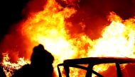 A rioter is seen near a burning car at the 