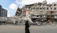 A Palestinian woman carrying her son flees her home during Israeli air and artillery strikes, as she walks near the site of a tower building destroyed in earlier strikes in Gaza City May 14, 2021. REUTERS/Mohammed Salem
