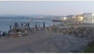 Migrants, who swam from Morocco to Spain, cross a fence on a beach in El Tarajal, Ceuta, Spain, May 17, 2021, in this still image from video obtained via social media. Ceuta Actualidad TV