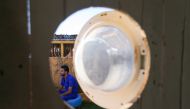 Palestinian artist, Ali Mhana, is seen through a glass door of a washing machine that he used as a window of a his makeshift office at an environment-friendly beachfront cafe in Gaza July 8, 2021. Picture taken July 8, 2021. REUTERS/Ibraheem Abu Mustafa