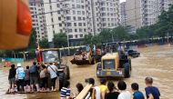 People ride on front loaders as they make their way through a flooded road following heavy rainfall in Zhengzhou, Henan province, China July 23, 2021. REUTERS/Aly Song