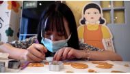 A customer uses a tool to cut a biscuit into a shape during a session of a South Korean Netflix show Squid Game-themed confection-making event, at a bakery in Beijing, China in this screengrab from a video taken on October 16, 2021. REUTERS TV via REUTERS