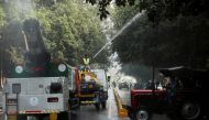 A vehicle with an anti smog gun passes by as a labourer sprinkles water using a tanker to settle dust and to curb air pollution in New Delhi, India, November 8, 2021. REUTERS/Anushree Fadnavis