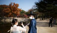 A couple dressed in Korea's traditional Hanbok costume, wearing protective face masks to avoid contracting the coronavirus, enjoy an autumn day at Gyeongbok palace in Seoul, South Korea, November 17, 2021. REUTERS/Kim Hong-Ji/File Photo