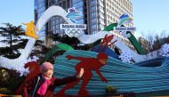 A woman poses for pictures in front of an installation featuring National Speed Skating Oval and logos of the Beijing 2022 Winter Olympics, in Beijing, China January 17, 2022. REUTERS/Tingshu Wang