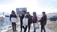 Syrian refugee children in Lebanon carry aid provided by QRCS.