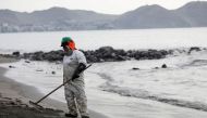 A worker cleans up an oil spill at the beach as demonstrators take part in a protest outside Repsol's La Pampilla refinery against the recent oil spill that has caused an ecological disaster on the coast of Lima, in Ventanilla, Peru January 29, 2022. REUTERS/Angela Ponce/File Photo