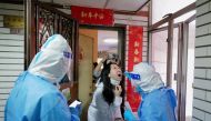 A worker in a protective suit collects a swab from a resident at a residential compound under lockdown, following the coronavirus disease (COVID-19) outbreak in Shenzhen, Guangdong province, China March 14, 2022. Picture taken March 14, 2022. cnsphoto via REUTERS