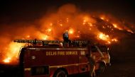 A firefighter uses his mobile phone as he sits on top of a fire truck as smoke billows from burning garbage at the Bhalswa landfill site in New Delhi, India, April 27, 2022. REUTERS/Adnan Abidi