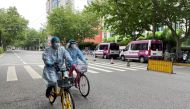 Workers in protective suits ride bicycles on a street amid a coronavirus disease (COVID-19) outbreak, during the Labour Day holiday in Shanghai, China April 30, 2022. REUTERS/Brenda Goh